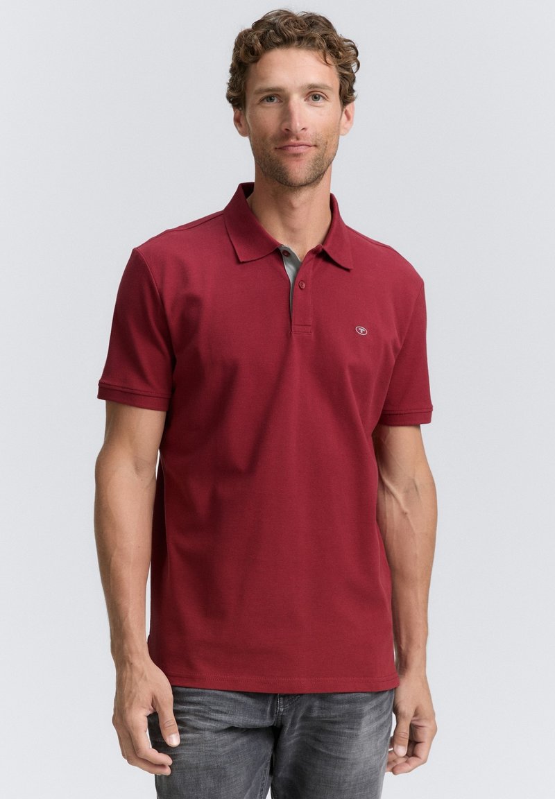 Camisa polo roja con un cuello gris, con mangas cortas y un cuello abotonado. La tela parece suave con una textura sutil.