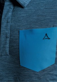 Kortärmad polo med strukturerad mörkblåt tyg, som har en enfärgad ljusblå ficka med en logotyp. Detalj av knappkrage synlig.