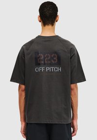 Mørkegrå bomulds T-shirt med korte ærmer, med et stort grafisk tryk på ryggen i sort og brun, med teksten "223 OFF PITCH."