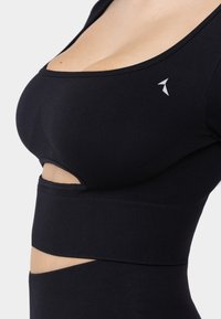 Crni atletski crop top s izrezom, izrađen od rastezljivog materijala. Ima okrugli izrez i mali logo na prsima.