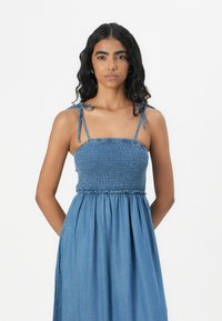 Denim maxi-kjole med strikket bodice, justerbare skulderbånd og full skjørt. Stoffet er mykt med en lys blå nyanse, og har en flytende design.