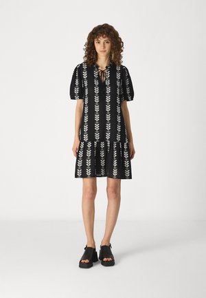 Black dress with white leaf pattern, short puff sleeves, and a tiered skirt. Paired with black open-toe platform shoes.