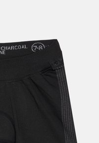 Artimiausiai juodų sportinių šortų nuotrauka su elastine juosta, pažymėta dydžiu 7-8, ir snapais šoniniame siūle.