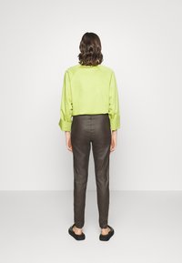 Camisa verde limão curta com mangas longas; combinada com calças justas castanhas escuras. Texturas suaves; a pessoa usa sapatos pretos.