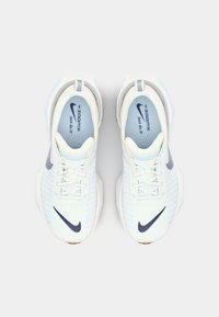 White athletic shoes with a mesh upper, light blue accents, and a dark blue Nike swoosh. Features cushion sole and lace-up design.