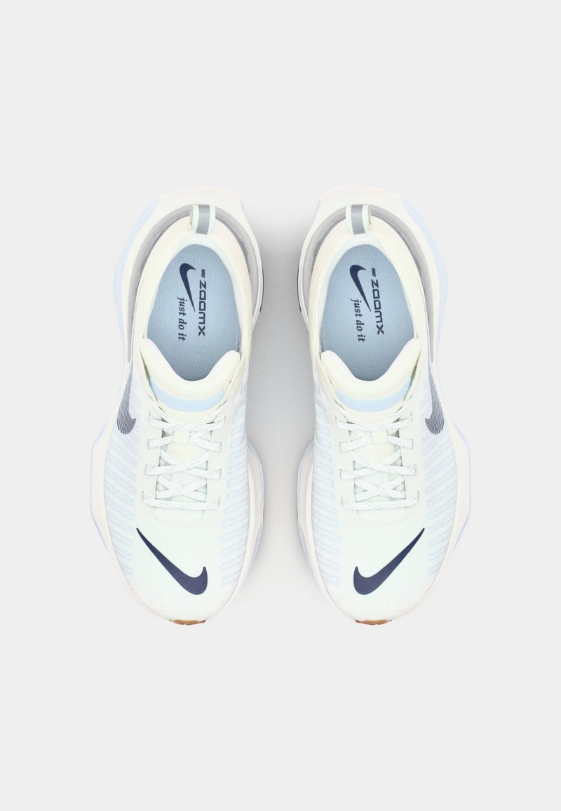 Zapatillas deportivas blancas con parte superior de malla, acentos en azul claro y un logo de Nike en azul oscuro. Presentan una suela acolchada y un diseño con cordones.