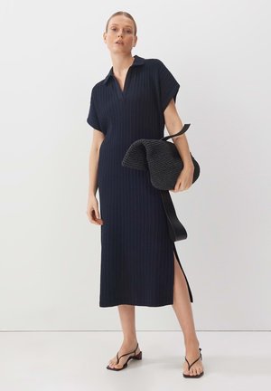 Abito a coste blu navy con maniche corte e colletto, spacco laterale, abbinato a una borsa nera testurizzata e sandali neri con cinturini.