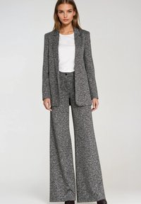 Czarnobiały garnitur w kratę pepitkę z dopasowaną marynarką i szerokimi spodniami. Materiał wydaje się mieć fakturę, pod spodem gładki biały top.