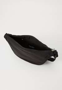 Bolsa de mão preta em nylon com uma textura suave, fecho com zipper e um rótulo interior. Apresenta uma forma compacta e aerodinâmica.