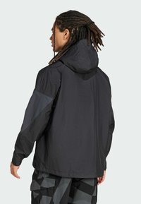 Giacca nera impermeabile con cappuccio, dotata di dettagli grigi sulle maniche, vestibilità rilassata e texture liscia. Design minimalista.