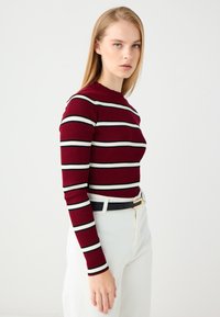 Maglietta a maniche lunghe a coste in bordeaux con righe orizzontali nere e bianche. Presenta un collo rotondo e una silhouette aderente.