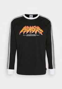 Svart långärmad skjorta med vita manschetter och tre vita ränder på ärmarna. Har en livlig orange grafisk logotyp i centrum.