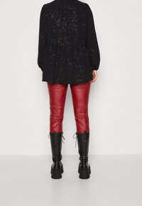 Haut peplum noir avec des paillettes métalliques, associé à un pantalon en cuir rouge et des bottes noires montantes à talon épais avec des accents en dentelle.