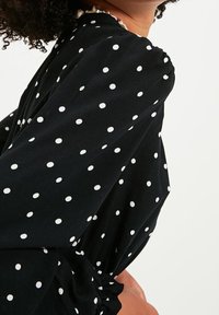 Blusa nera a pois con maniche lunghe, caratterizzata da macchie bianche, un dettaglio con maniche arricciate e una texture morbida e fluida.