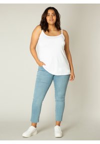 Witte mouwloze tanktop, lichtblauwe skinny jeans, witte sneakers. Glad materiaal, casual ontwerp, aansluitende pasvorm, ruwe zoomdetails op de jeans.