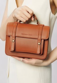 Brązowa skórzana torebka o strukturalnym designie, z dwiema górnymi rączkami, złotymi akcentami oraz wytłoczonym logo z przodu.