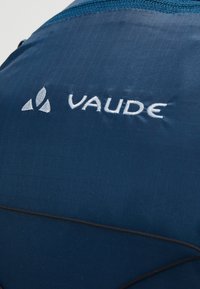 Zaino di colore blu scuro con finitura testurizzata. Presenta un logo "VAUDE" bianco ben visibile e dettagli accentuati in nero.