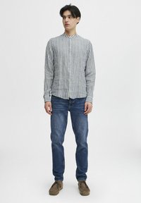 Camisa de botón a rayas en azul y blanco, combinada con jeans azules y zapatos marrones. Mangas largas, corte ajustado, diseño minimalista.