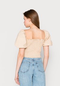Haut crème ajusté à manches courtes avec un corsage smocké et un décolleté carré ; associé à un jean bleu clair taille haute.