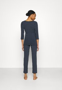 Marinblå prickig jumpsuit med trekvartslånga ärmar, figurnära design och ankellånga ben. Slät tyg, rund halsringning, inga knappar.