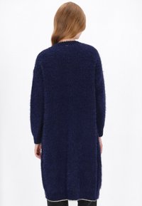 Hosszú, sötétkék, bolyhos kötött kardigán, laza szabással, kerek nyakkivágással és hosszú ujjal, ezüst díszítéssel ellátott hem kávéval.