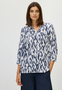 Blusa de patrón en navy y blanco con escote en V, mangas tres cuartos y corte holgado. Confeccionada en tela ligera con un diseño texturizado.