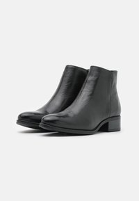 Botas negras de cuero hasta el tobillo con una textura suave, punta redonda y un tacón bajo tipo bloque. Presentan una lengüeta en la parte trasera para ponérselas con facilidad.