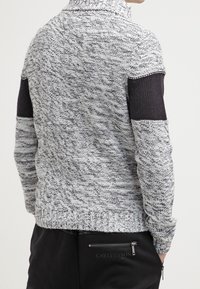 Grå och svart marmorvirkad tröja med hög krage, ribbade muddar och texturerade mönster på baksidan och ärmarna. Har en figurnära design.