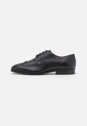 Black leather dress shoe with brogue detailing, lace-up design, rounded toe, and low stacked heel. Smooth texture with polished finish.