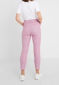 Roze gebloemde broeken met een getailleerd ontwerp, voorzien van een hoge taille, achterzakken en taps toelopende pijpen. Gecombineerd met een wit T-shirt en sneakers.