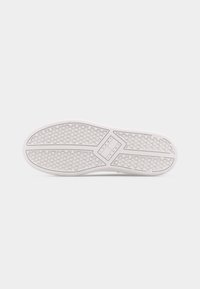 Σόλα ενός λευκού αθλητικού παπουτσιού με κυκλικό υφή μοτίβο λαβής και ορθογώνια περιοχή λογότυπου με την επισήμανση "Tommy Jeans" στο κέντρο.