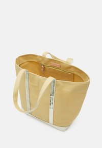 Beige kanvas toteväska med två handtag, vertikala ränder i silverpaljetter, ett internt dragkedjefack och en lädermärke inuti.