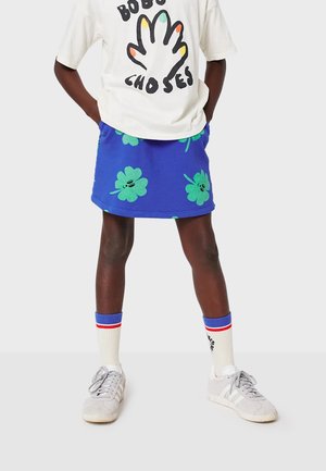 Blue skirt with green floral patterns, paired with a white graphic t-shirt, white and red striped socks, and gray sneakers.