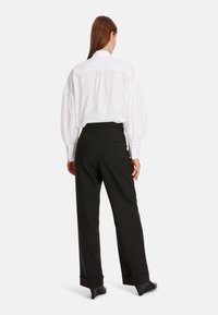 Weißes, übergroßes Hemd mit puffärmeln, Knopfmanschetten und hohem Kragen; kombiniert mit maßgeschneiderten schwarzen Hosen mit einem eleganten Design.