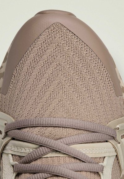 Light brown athletic shoe with a textured fabric upper, smooth toe cap, and flat laces, featuring neutral-toned accents and reinforced areas.