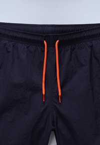 Jūriniai šortai su elastine juosmeniu ir ryškiai oranžinėmis raištelėmis, nenuskleidžiamu audiniu ir tekstūruotu paviršiumi.