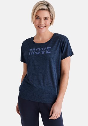 Blonde Frau lächelt, trägt ein marineblaues kurzärmeliges Shirt mit dem Text "MOVE KEEP ACTIVE" und dazu passende marineblaue Hosen vor weißem Hintergrund.