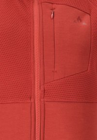 Röd atletisk zip-up jacka med strukturerad tyg, släta sektioner och en bröstficka med dragkedja. Dekorativ logotyp i övre hörnet.