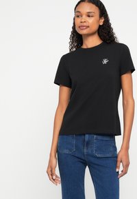 Tricou negru din bumbac, cu mânecă scurtă, guler rotund, având un mic logo alb brodat în zona buzunarului stâng.