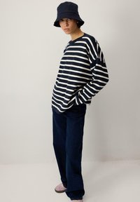 Pasiasta granatowo-biała koszula z długim rękawem w połączeniu z ciemnymi dżinsami oraz granatowym kapeluszem typu bucket, tworząc swobodny i casualowy zestaw.