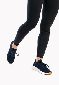 Scarpe da atletica blu navy con tomaia in knit texturizzato, design con lacci e suola intermedia bianca; abbinate a leggings neri aderenti.