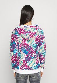 Hooded sweatshirt featuring a vibrant, multicolored leaf pattern in pink, blue, and cream on a white background. Soft, textured fabric.