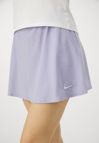 Falda deportiva de color púrpura claro con un diseño fluido, confeccionada en material suave. Presenta un pequeño logo blanco de Nike en el borde inferior.