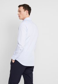 Lichtblauwe button-up overhemd met een textuurpatroon, lange mouwen en enkele manchetten. Gestyled met donkere broek, getoond vanaf de achterkant.
