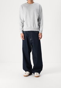 Sweat-shirt gris avec un col rond, associé à un jean en denim foncé ample. Des baskets blanches avec des accents beiges complètent la tenue.