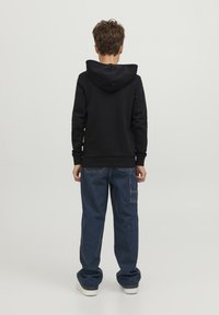 Sudadera negra con bolsillo canguro, capucha con cordón, combinada con unos vaqueros azul claros de corte holgado que tienen un bolsillo parche y los puños remangados.
