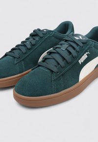 Sneaker in suede verde scuro con punta rotonda, suola in gomma marrone e accenti del logo Puma bianchi. Presentano lacci e un colletto imbottito per il comfort.