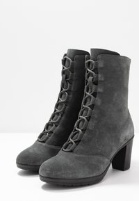 Stivaletti alla caviglia in suede grigio con tacco a blocco alto e design con lacci frontali. Presentano una texture liscia e una punta arrotondata con suola in gomma.