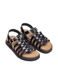 Sandalias de cuero negro con tiras, con una planta acolchada marrón, hebilla ajustable y una suela texturizada que presenta pequeños tachuelas en el borde.