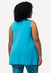 Una blusa sin mangas, de color azul, hecha de una tela suave, con un corte recto y aberturas laterales, combinada con leggings de color teal con estampado.